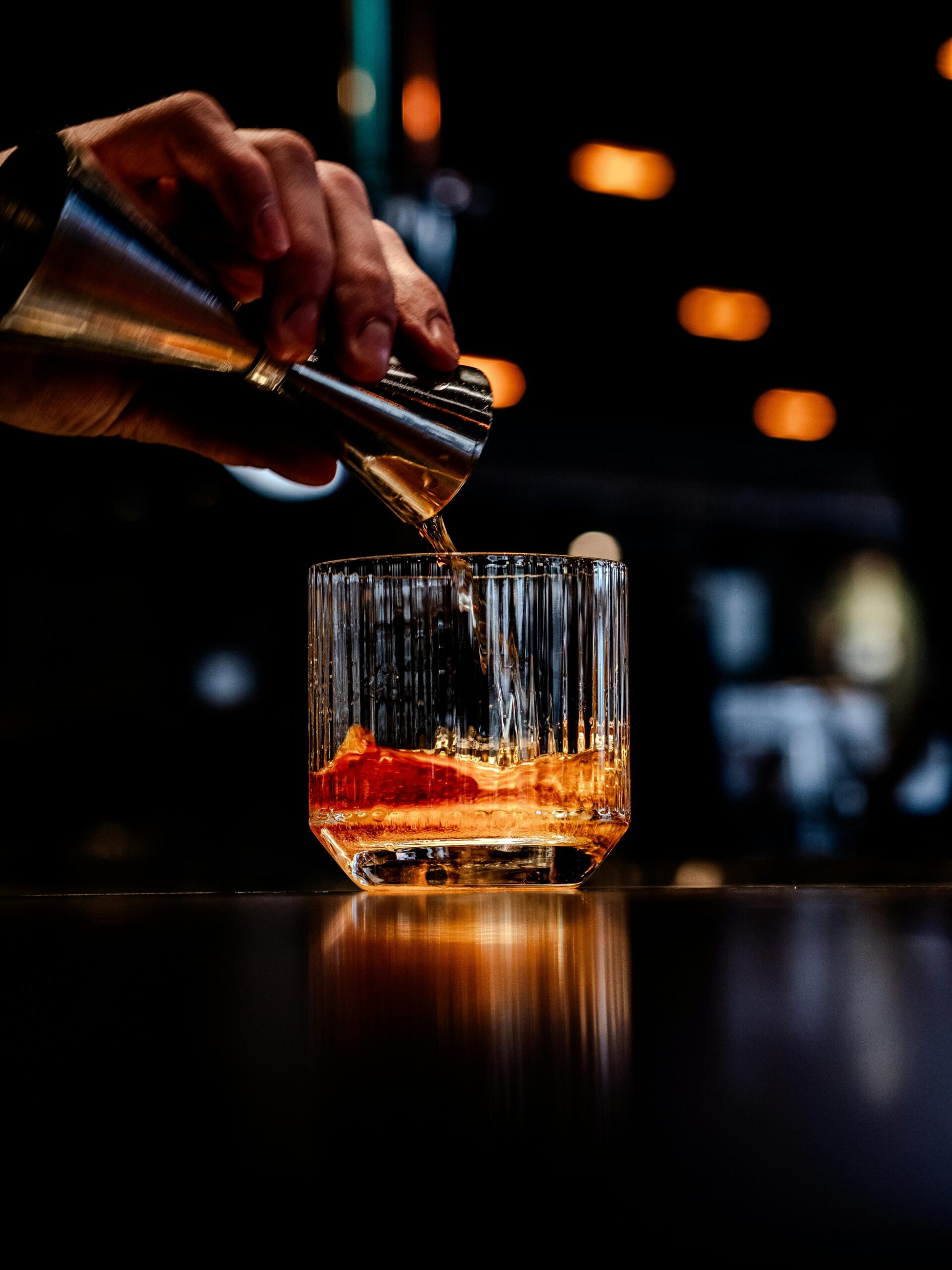 Elegant pour of whiskey into a glass with ice in a dimly lit bar setting.